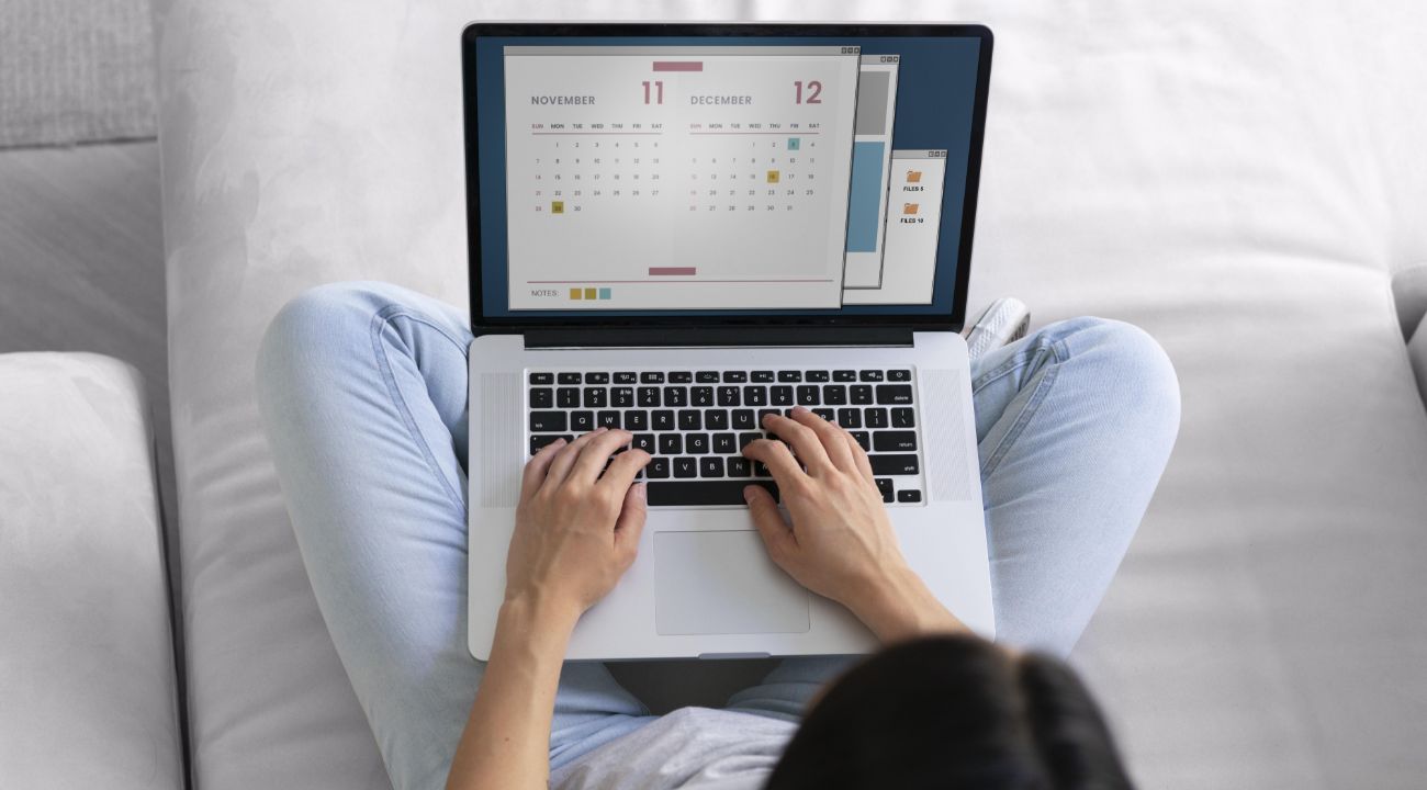 Woman working with planner and calendar on laptop from home Person using laptop with calendar and planner app organizing tasks and events from the sofa