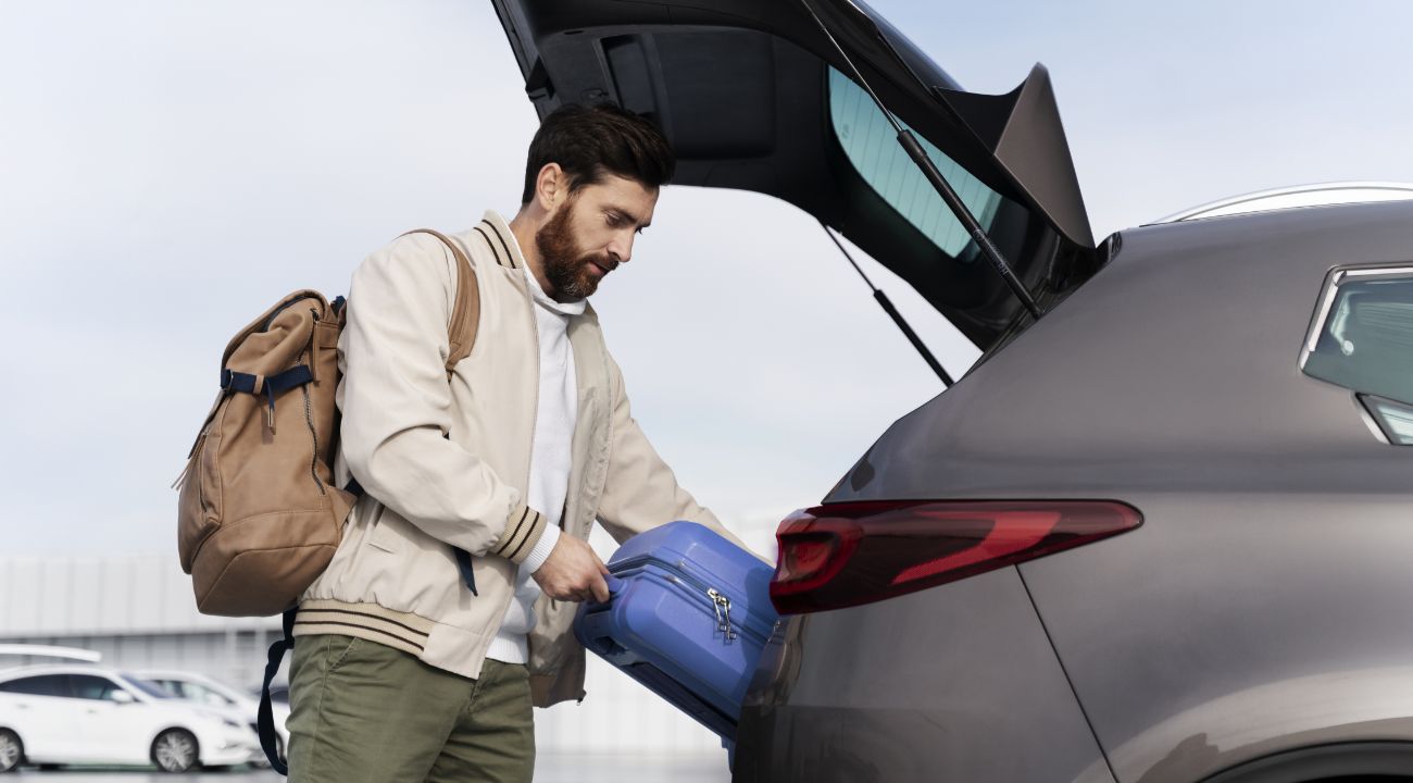 Traveler storing luggage in private transfer Man placing blue suitcase in vehicle trunk with backpack and travel luggage ready for transfer