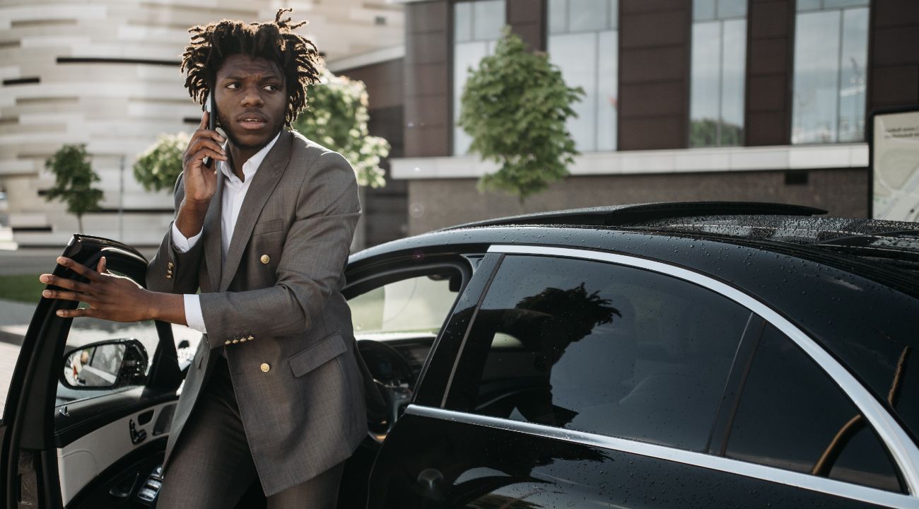Professional in suit organizing trip from luxury vehicle, working during transfer with phone call